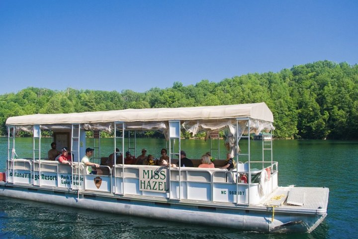 Tour boat on a lake with people onboard and green forest in the background.
