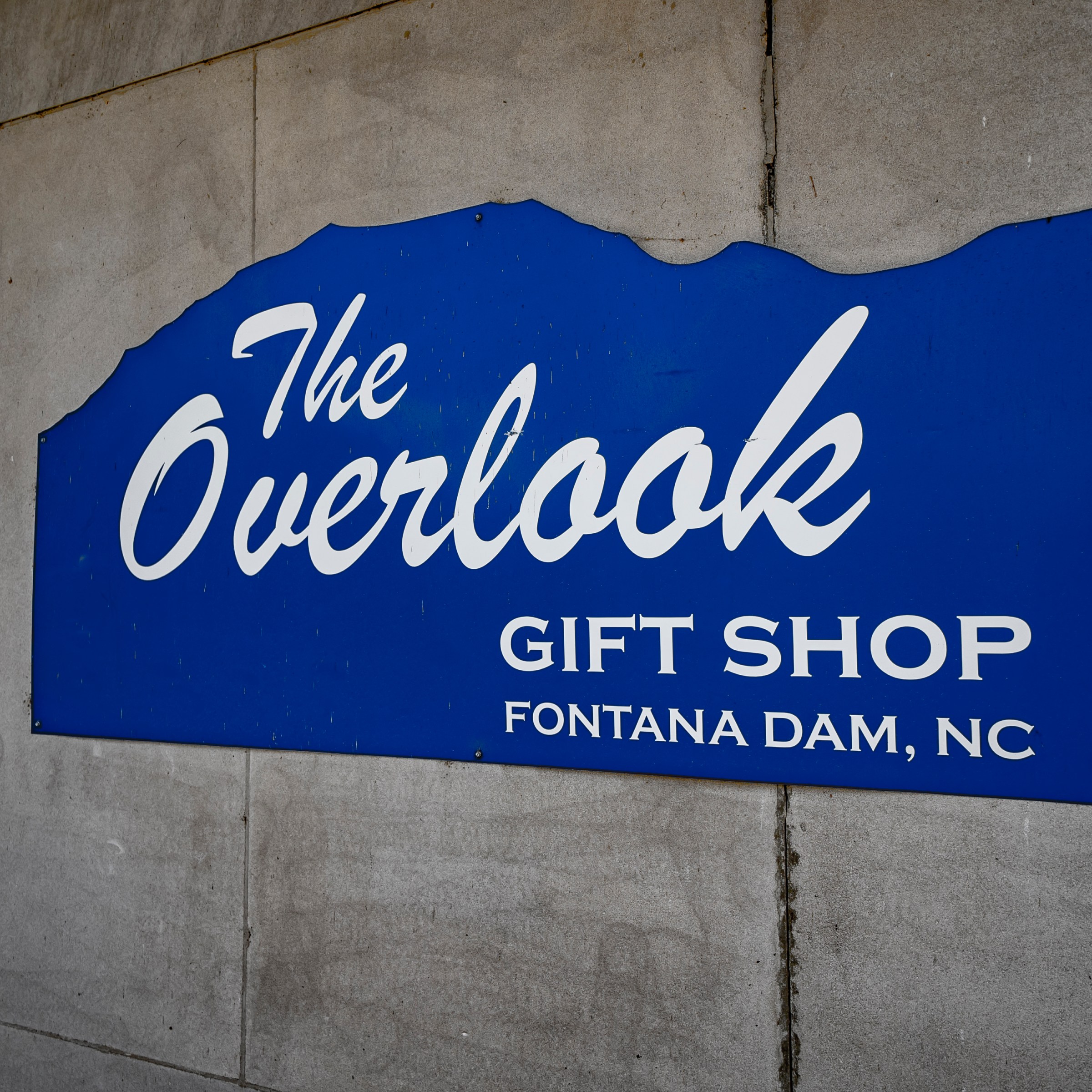 Blue sign for 'The Overlook Gift Shop' at Fontana Dam, NC on a concrete wall.