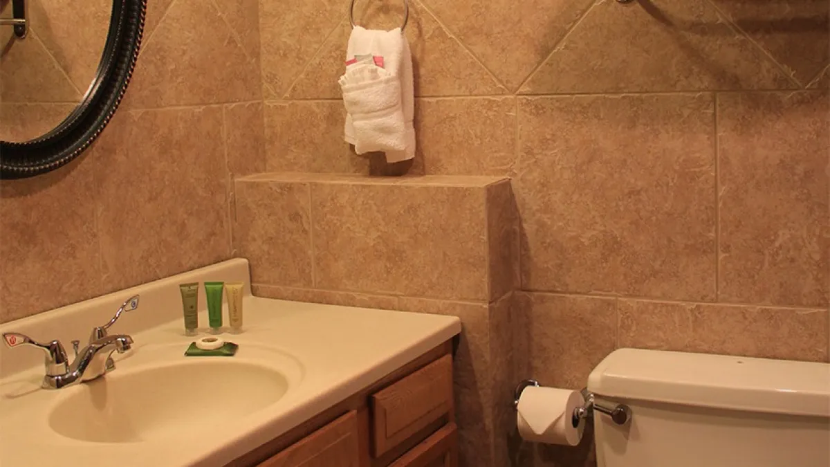 Bathroom with a sink, mirror, towel, and toilet on a tiled wall.