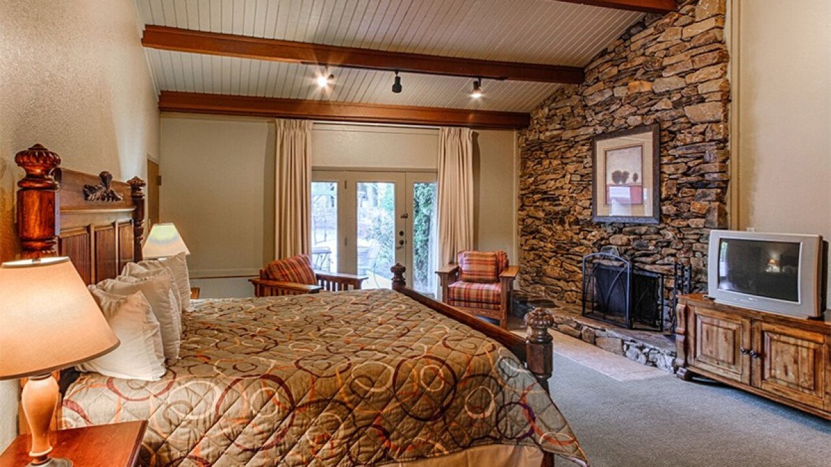 Cozy bedroom with a stone fireplace, wooden bed, and vintage TV, enhanced by natural light from French doors.