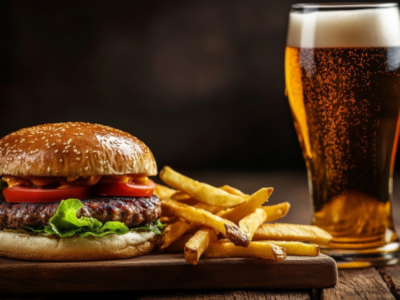 Burger with lettuce, tomato, fries, and a pint of beer on a wooden board.