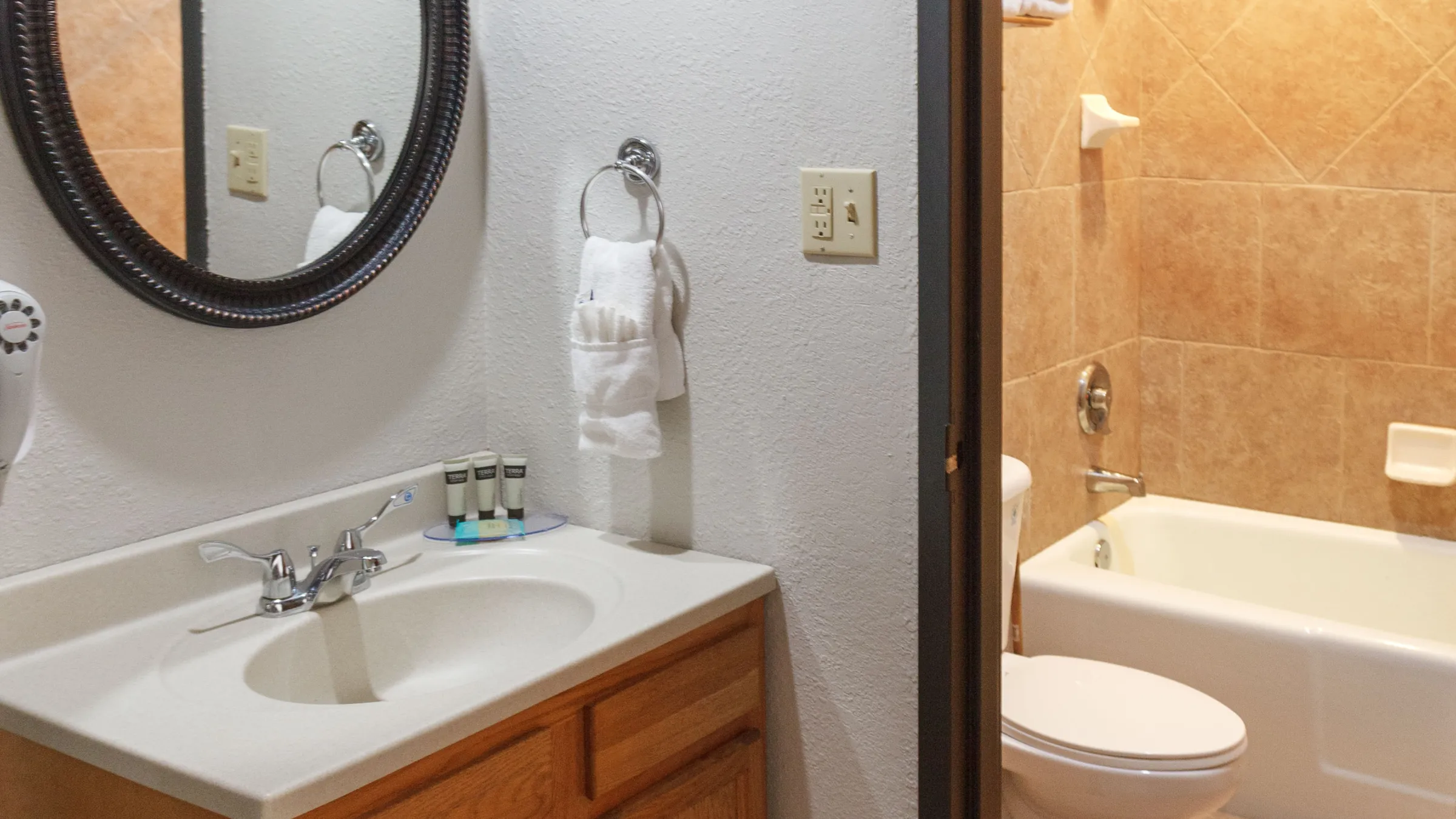 Bathroom with wooden vanity, round mirror, and towel holder beside a bathtub with tiled walls.