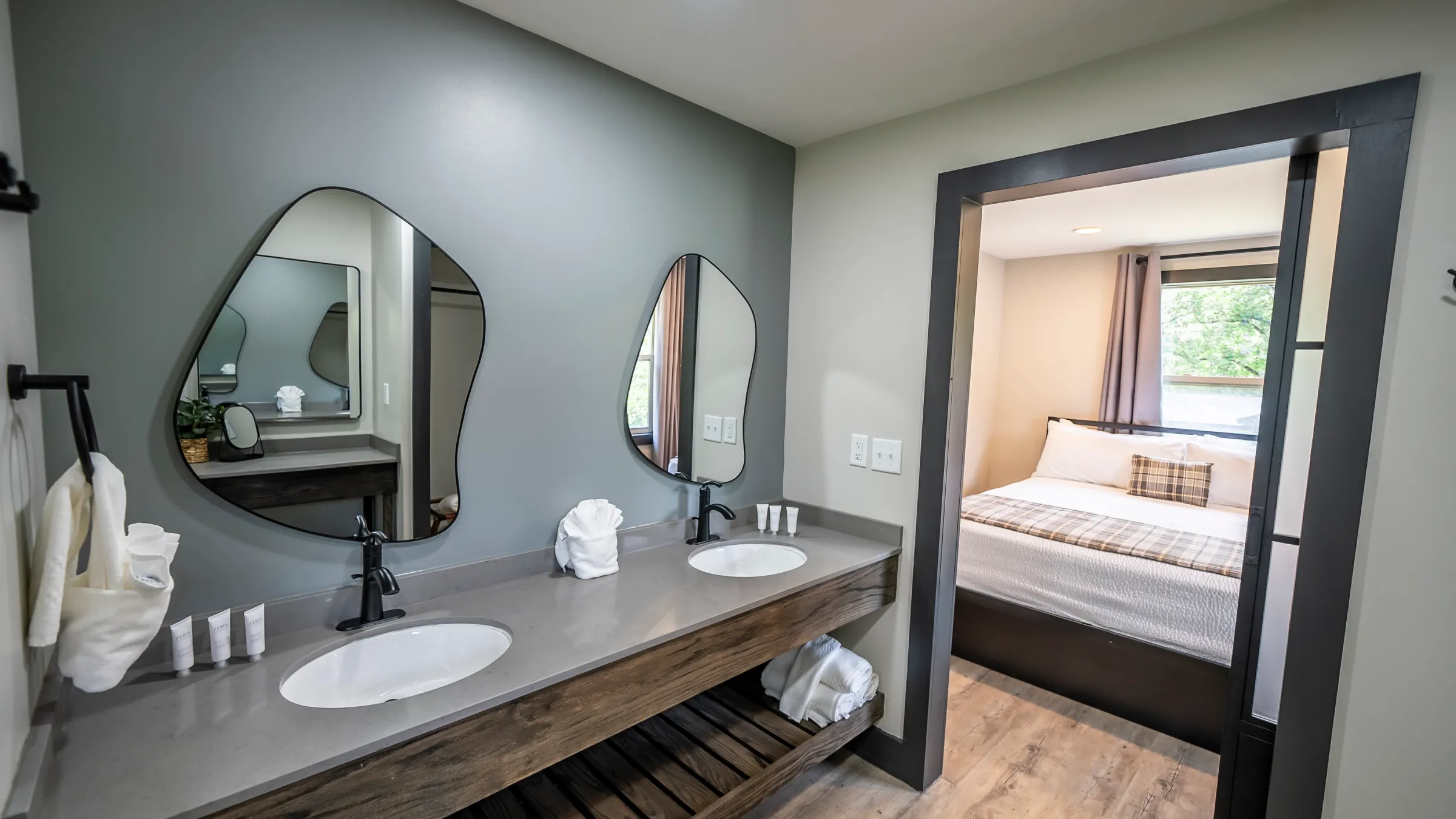 Modern bathroom with two sinks and a view into a bedroom.