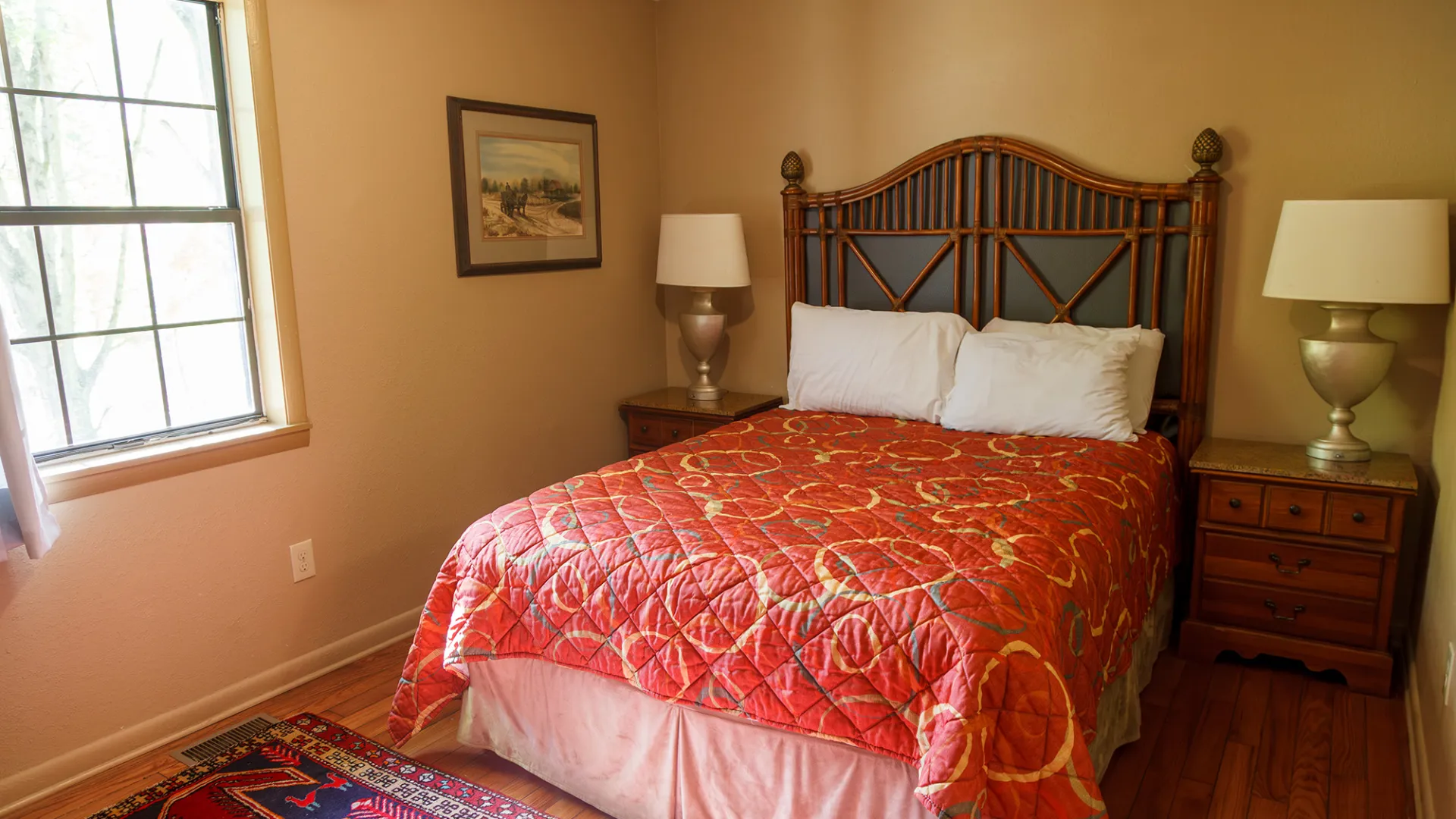 Cozy bedroom with wooden bed, two lamps, and a red quilted blanket on a hardwood floor.