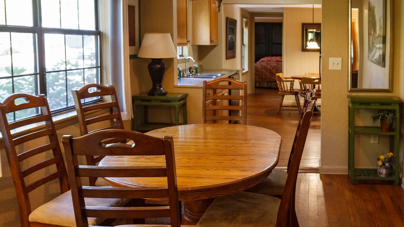 Dining room with wooden table, chairs, chandelier, wood floors, window, and entry to kitchen.