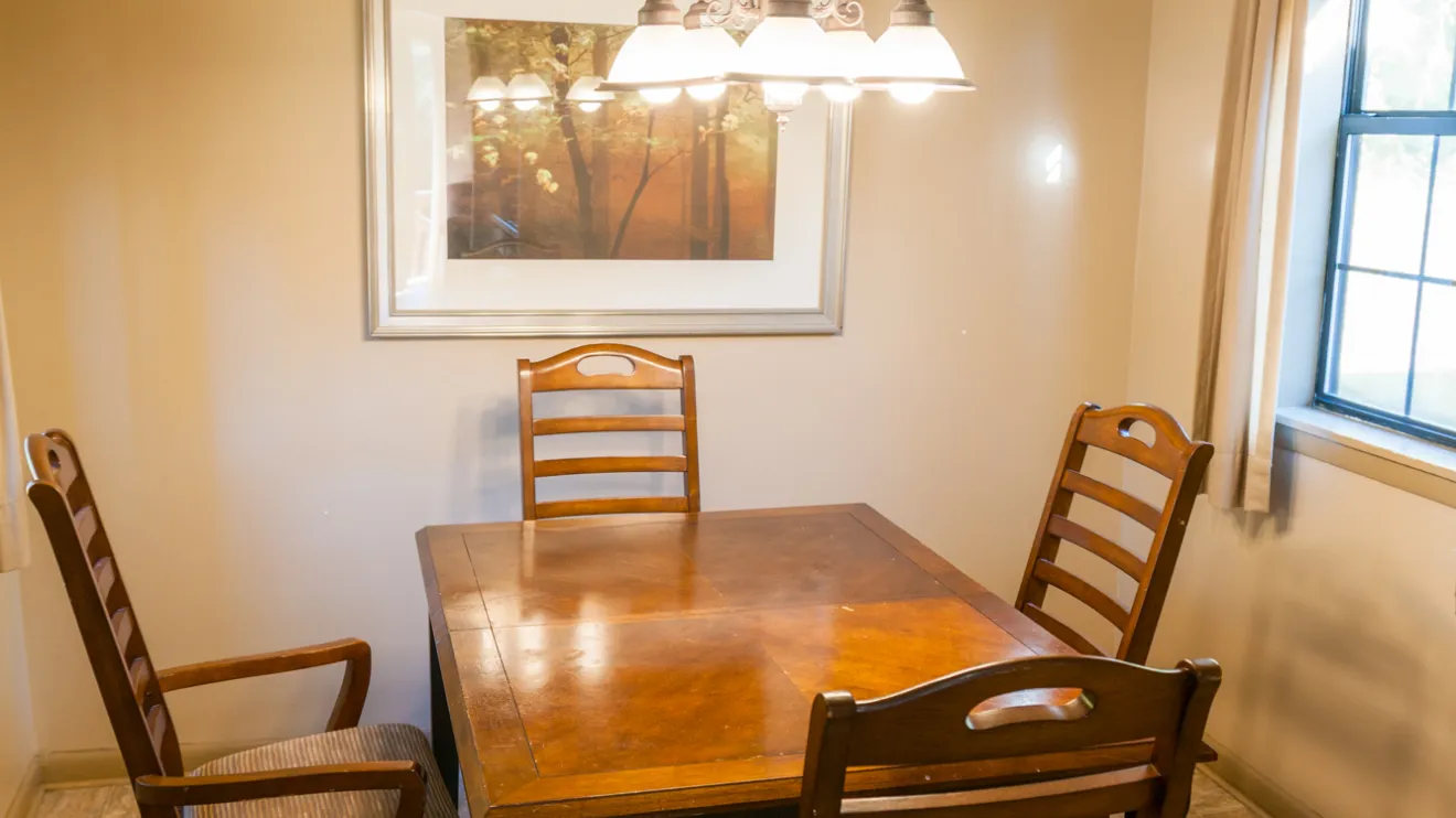 Dining room with a wooden table, four chairs, a hanging light, and a framed picture on the wall.
