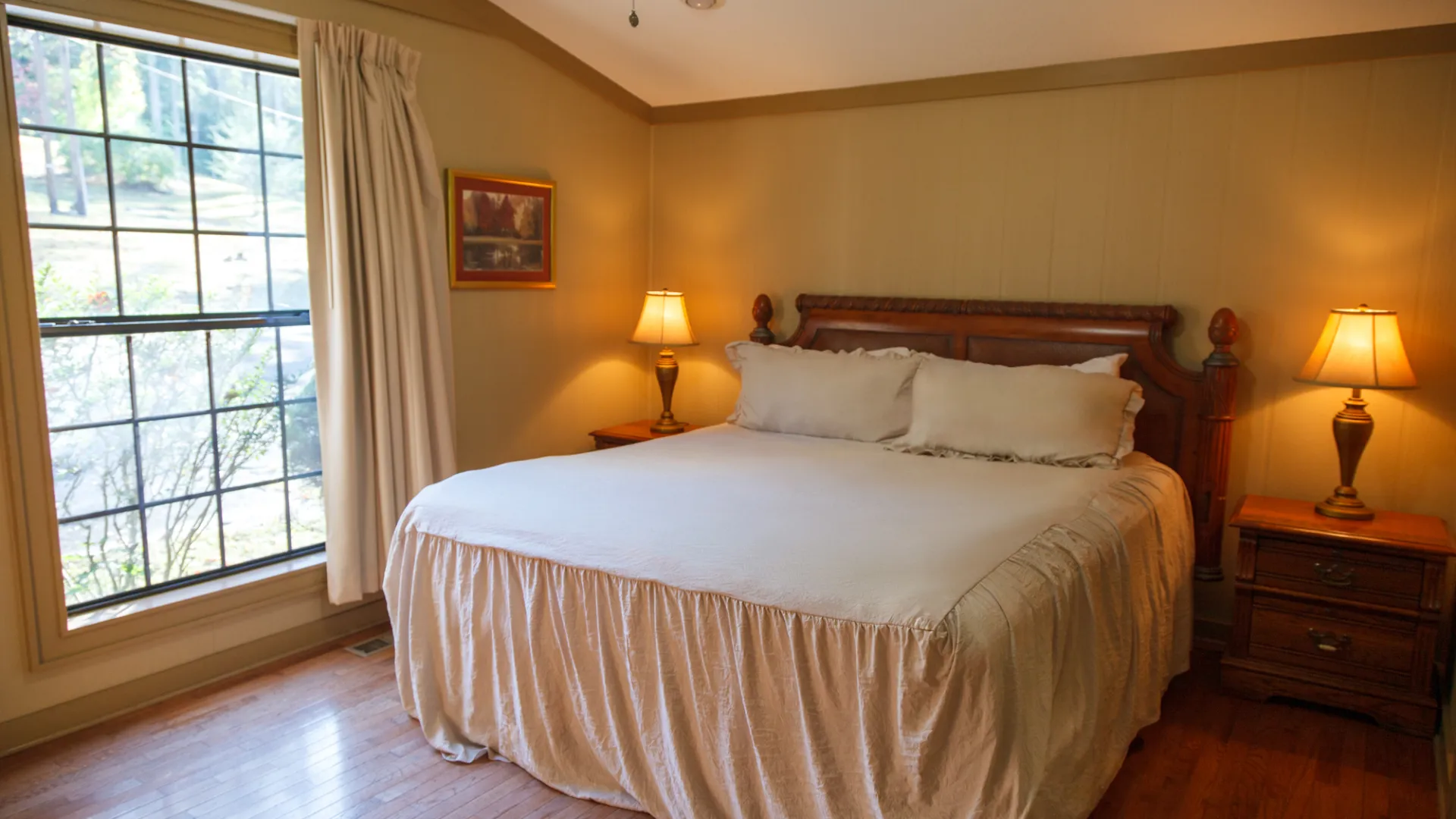 Cozy bedroom with a large bed, two lamps, and a window with curtains.