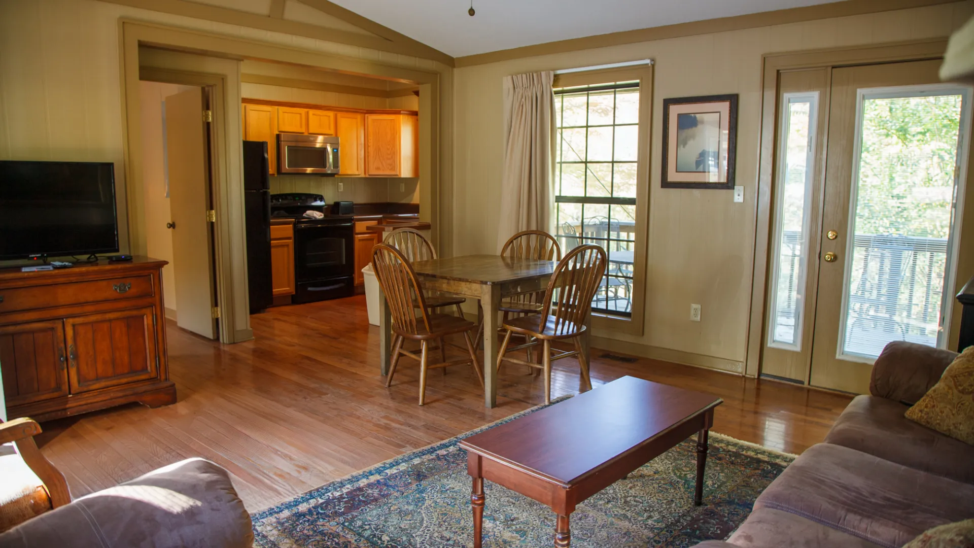 Cozy living room with sofa, TV, dining table, and kitchen in open layout with wooden flooring.