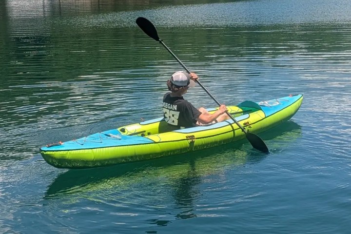 Person kayaking on a calm lake near a forested shore.