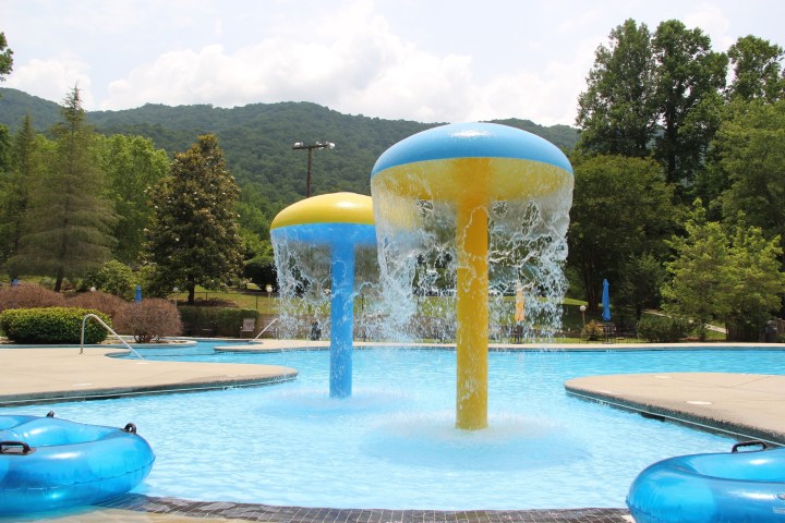 Outdoor pool with mushroom-shaped water fountains and mountains in background.