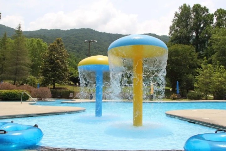 Outdoor pool with two mushroom fountains and inflatable tubes.