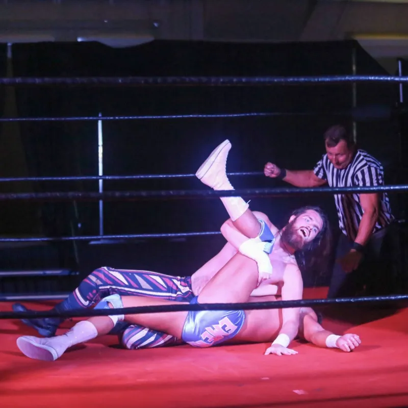Two wrestlers in a ring, one pinning the other, referee kneeling nearby.